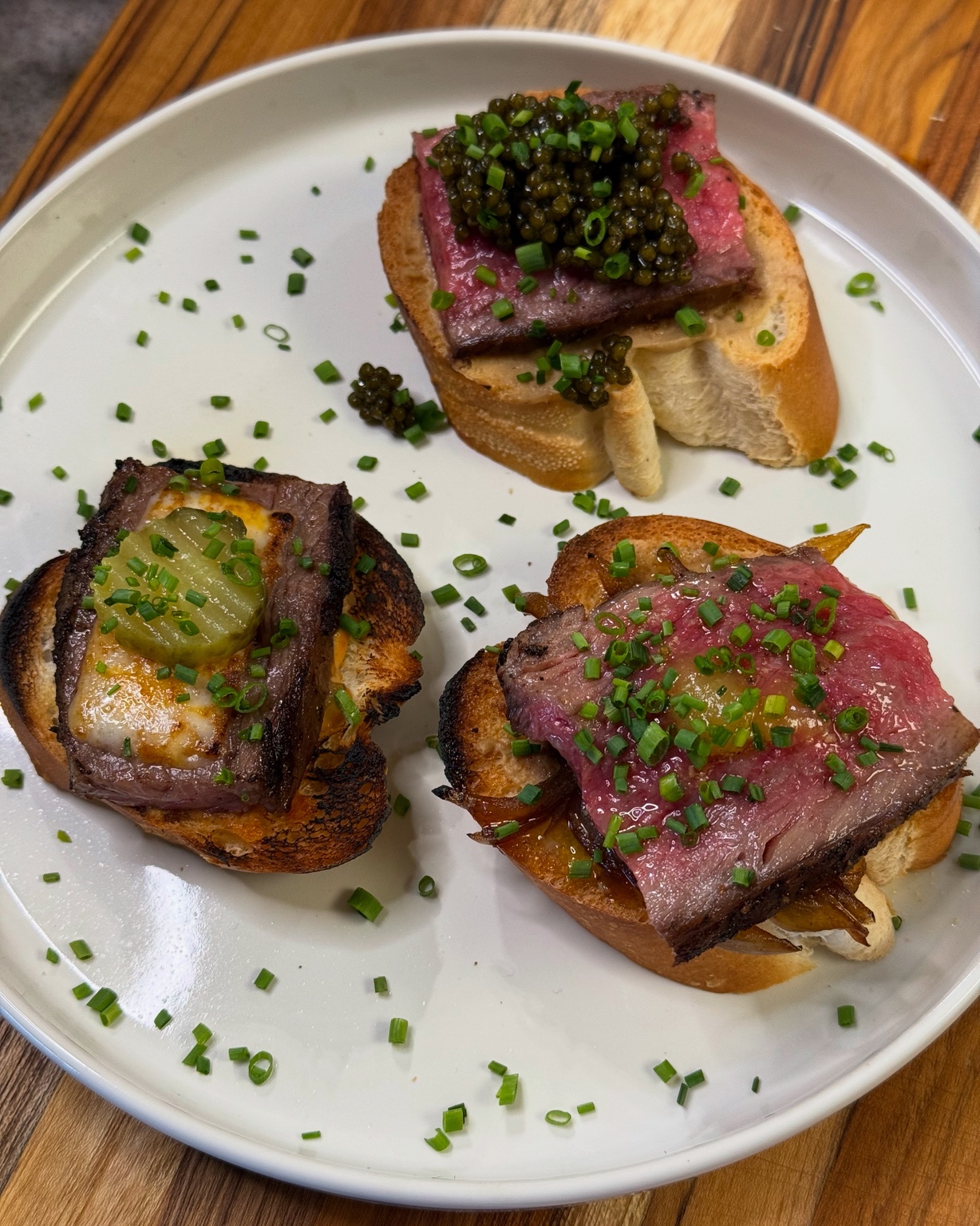 Three garnished steak toasts on a white plate